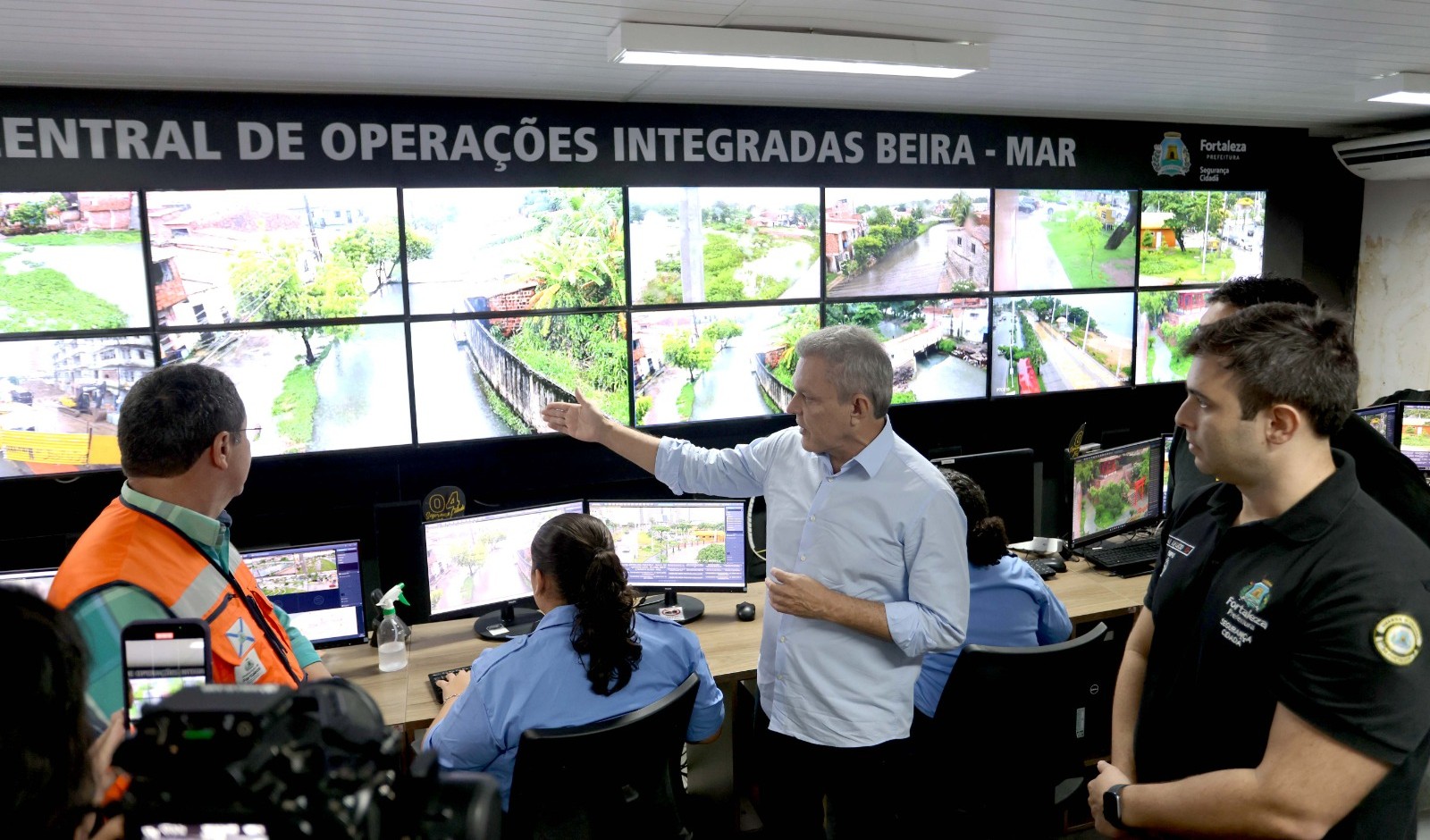 pessoas na sala de videomonitoramento diante das câmeras